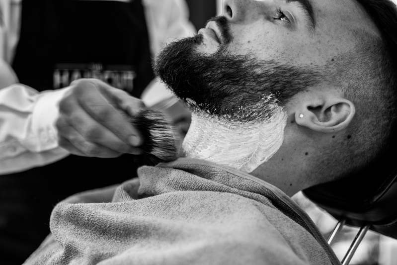 Close-up of hand holding professional beard scissors against a beard